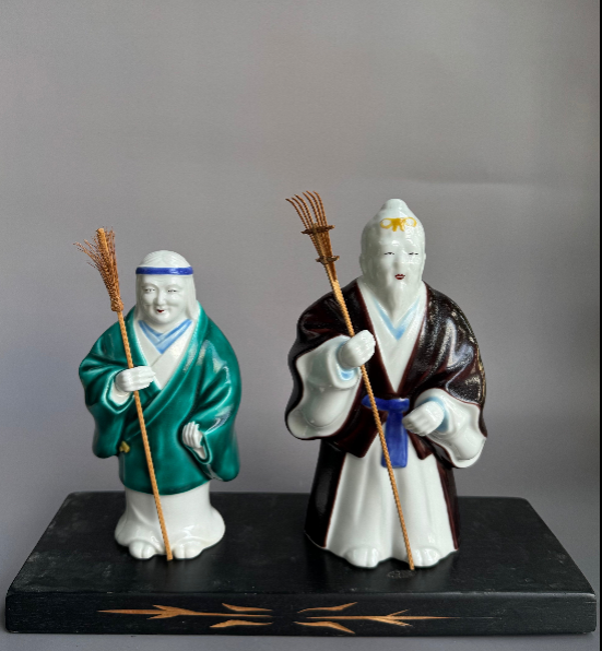 Pair of Japanese ceramic figurines holding bamboo rakes on black base