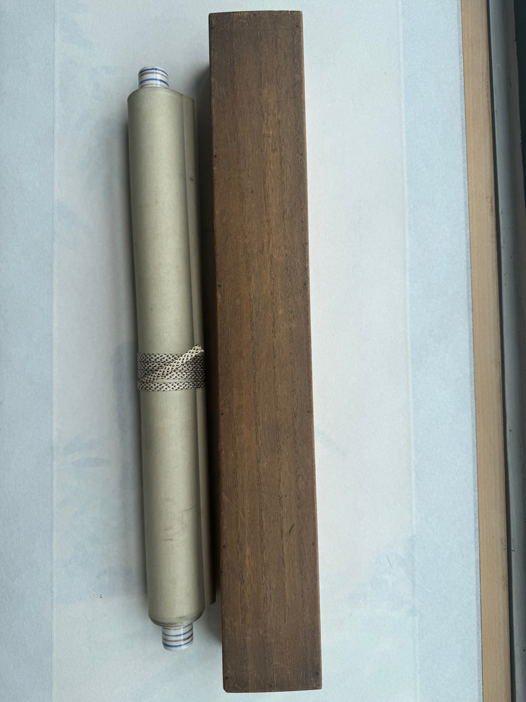Metallic cylindrical object with decorative band on a wooden block against a light blue background