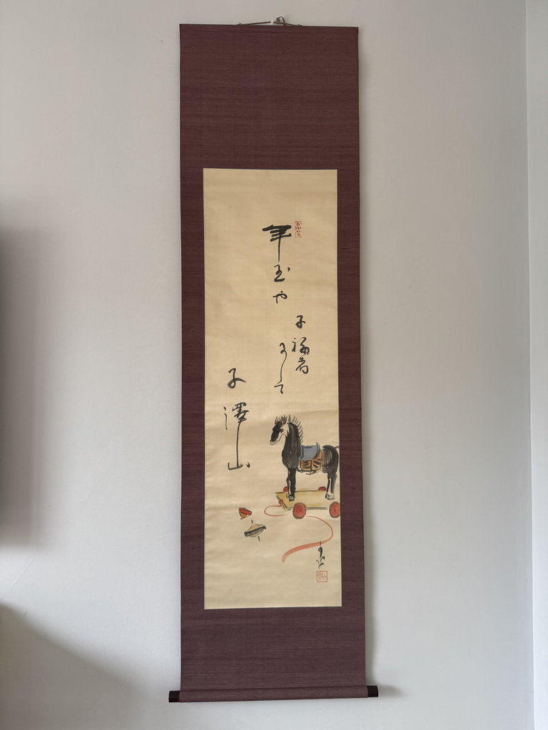 Traditional Japanes scroll with horse illustration and calligraphy on a plain wall.