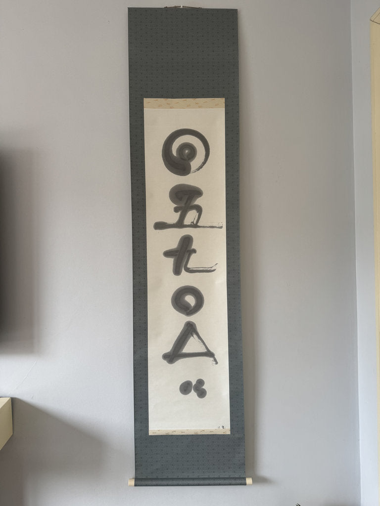 Vertical scroll with calligraphy on a plain wall