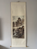 Traditional Japanes landscape painting on a vertical scroll hanging on a wall.