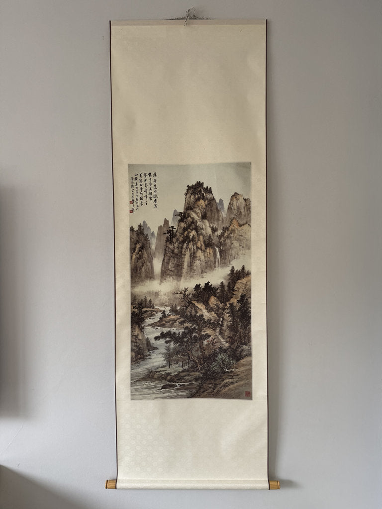 Traditional Japanes landscape painting on a vertical scroll hanging on a wall.