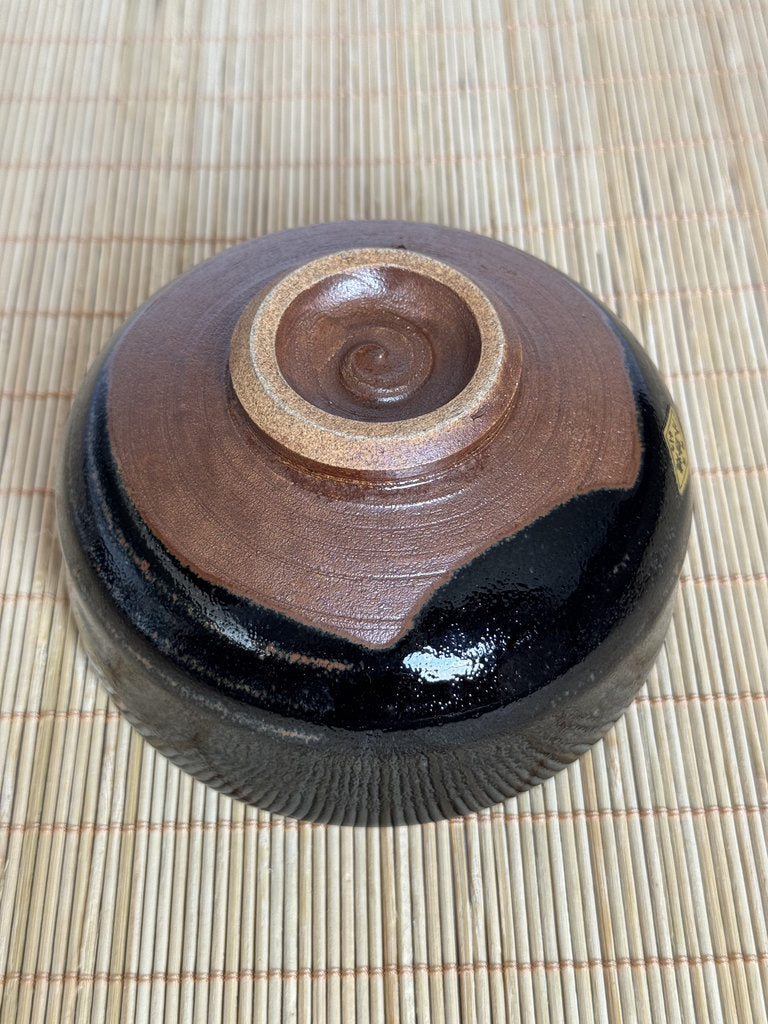 Ceramic container with brown and black design on a woven mat