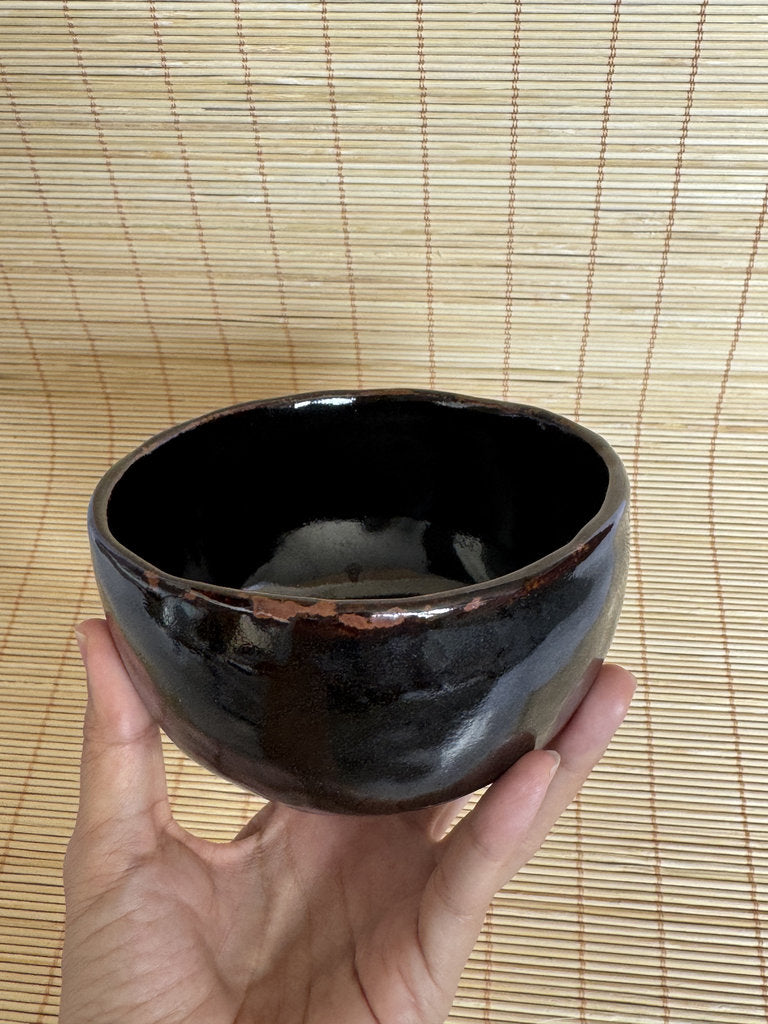 Black ceramic bowl held in a hand against a woven mat background