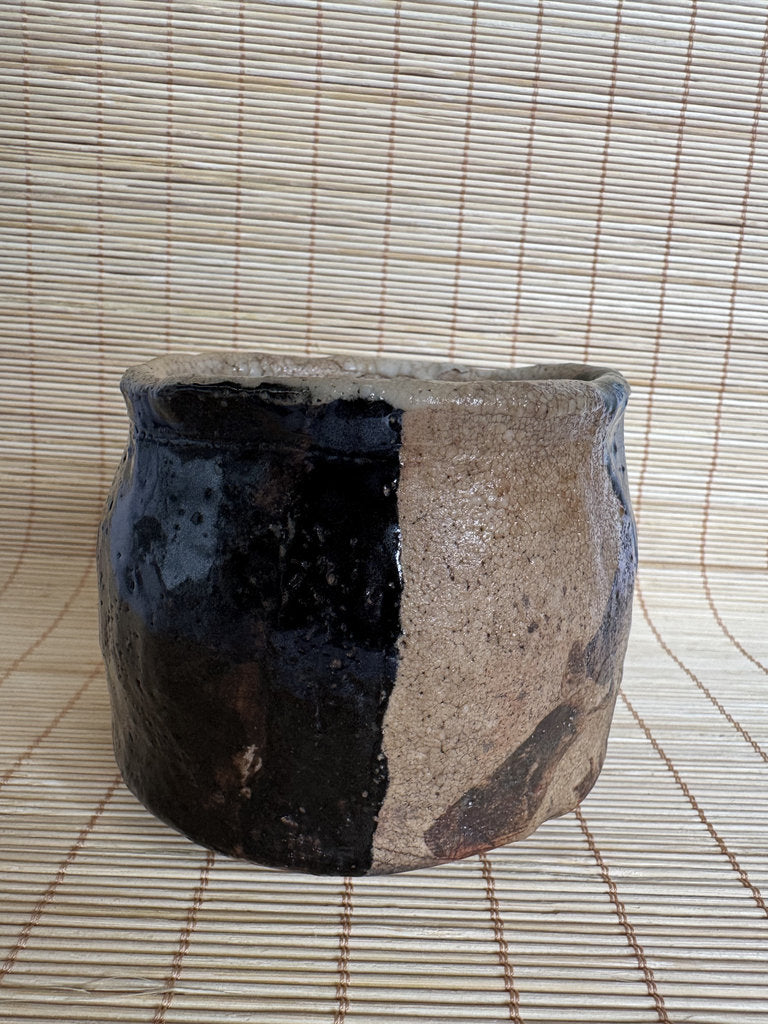 Ceramic pot with black and beige design on a woven mat background