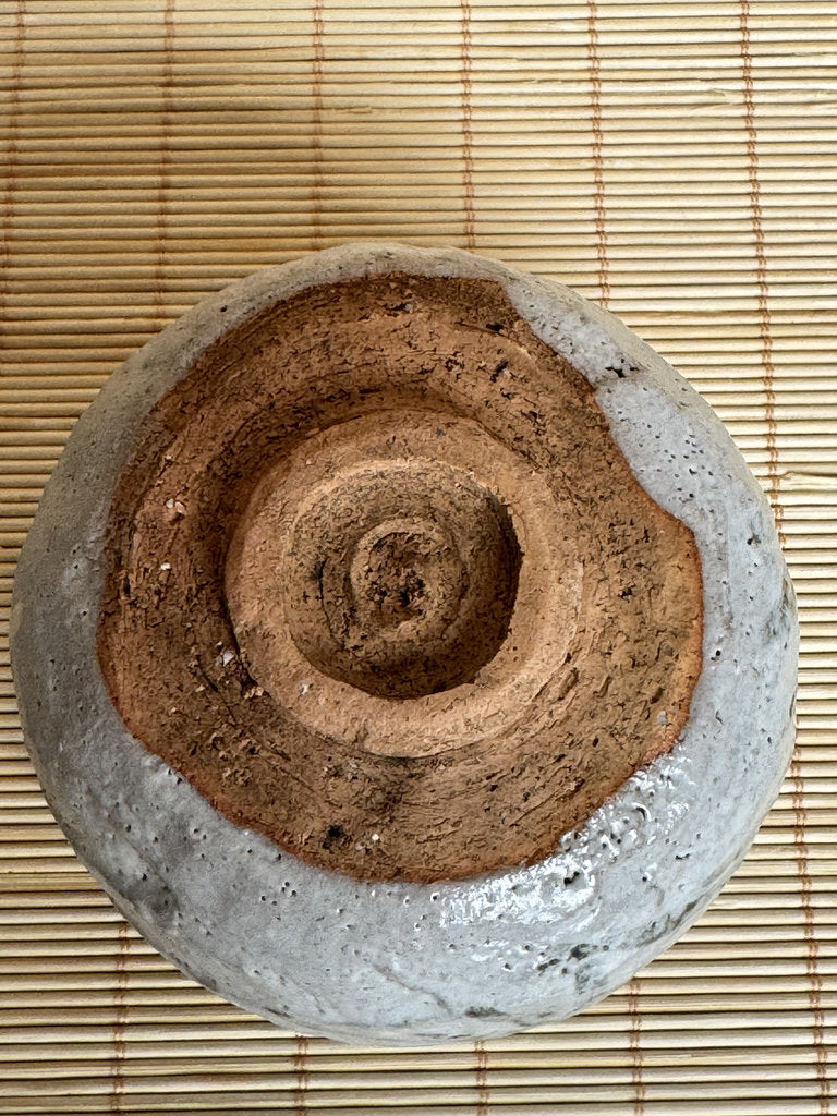 Ceramic bowl with concentric spiral design on a bamboo mat