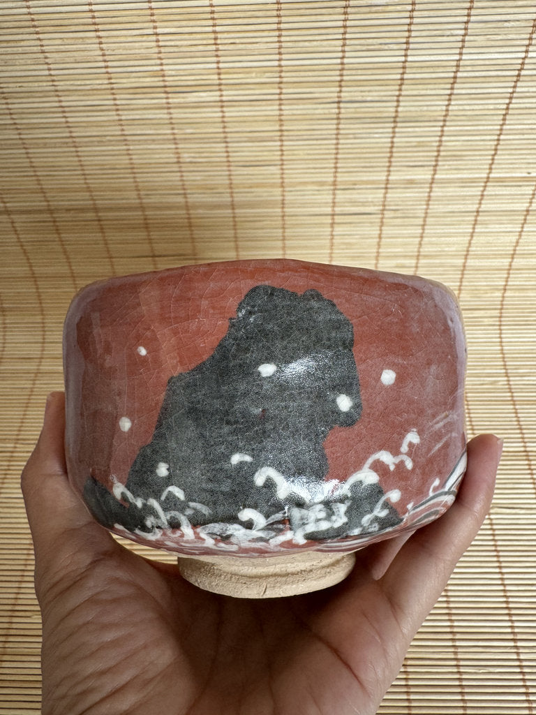 Ceramic bowl with a black bear design held by a hand on a woven mat background