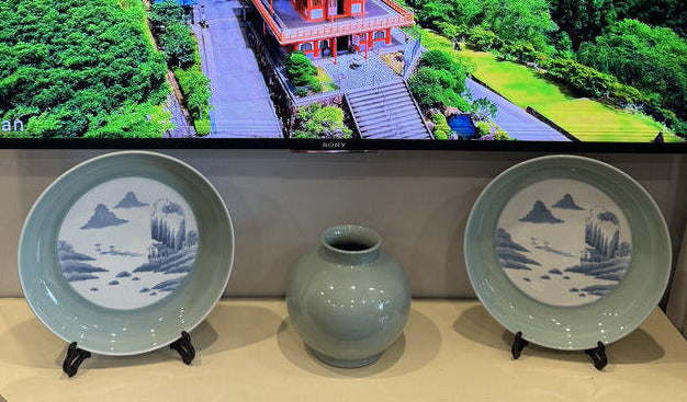 Television displaying a scenic landscape with two decorative plates and a vase on a stand.