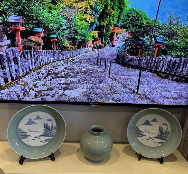 Television displaying a scenic landscape with two decorative plates and a vase on a stand.