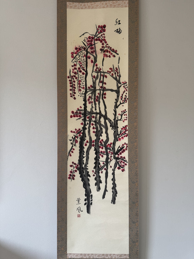 A traditional Japanese hanging scroll painting depicting red blossoms on dark branches, mounted on a light wall.