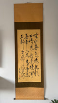 Roll of calligraphy on a wooden frame against a plain wall