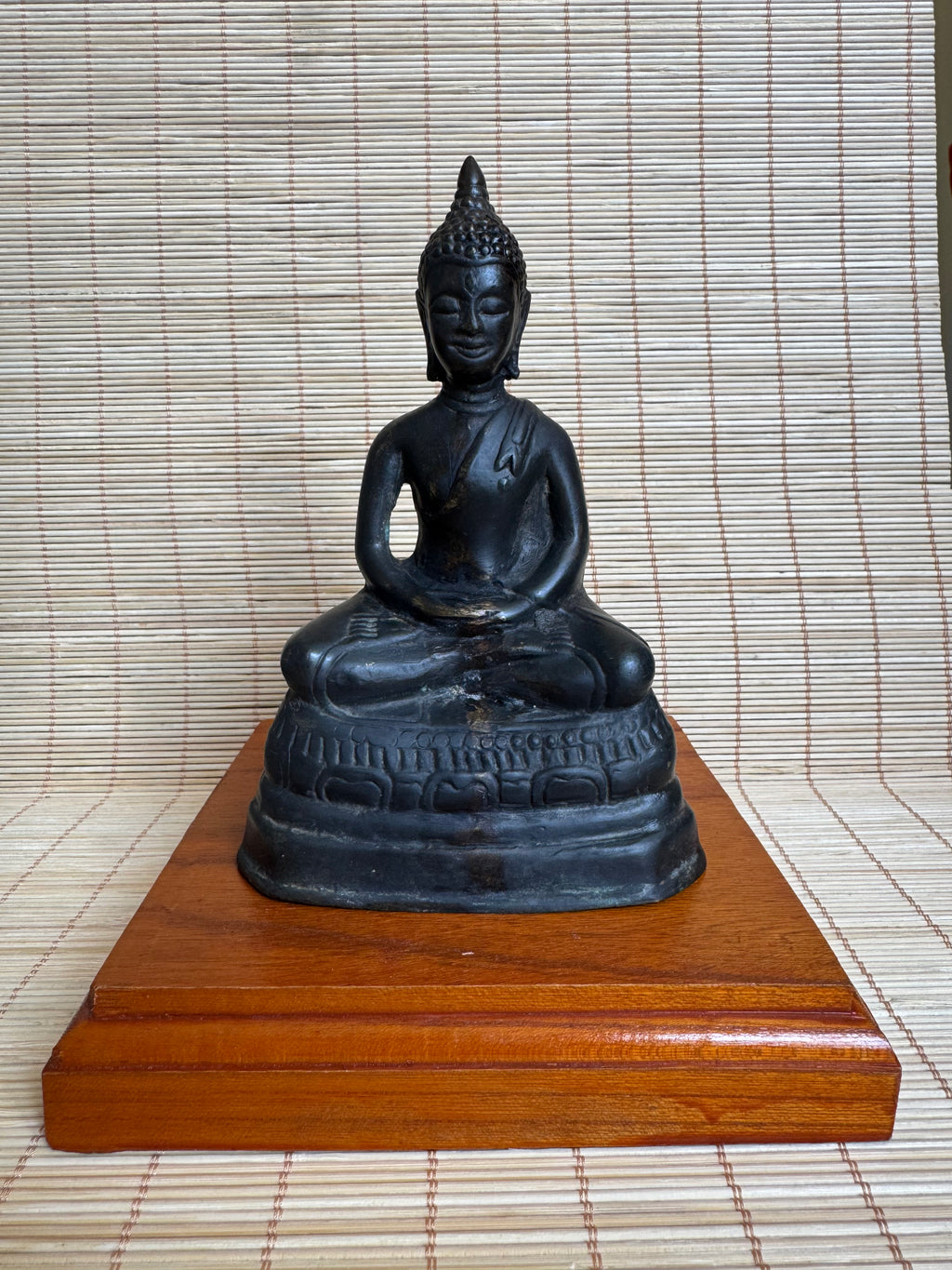 Black Buddha statue on a wooden stand against a woven mat background
