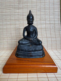 Black Buddha statue on a wooden stand against a woven mat background