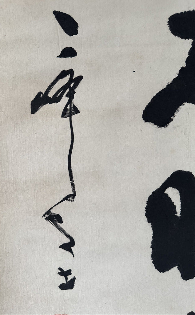 Close-up of a black ink calligraphy artwork on off-white paper, showing bold brushstrokes and a blue patterned border along the left edge.