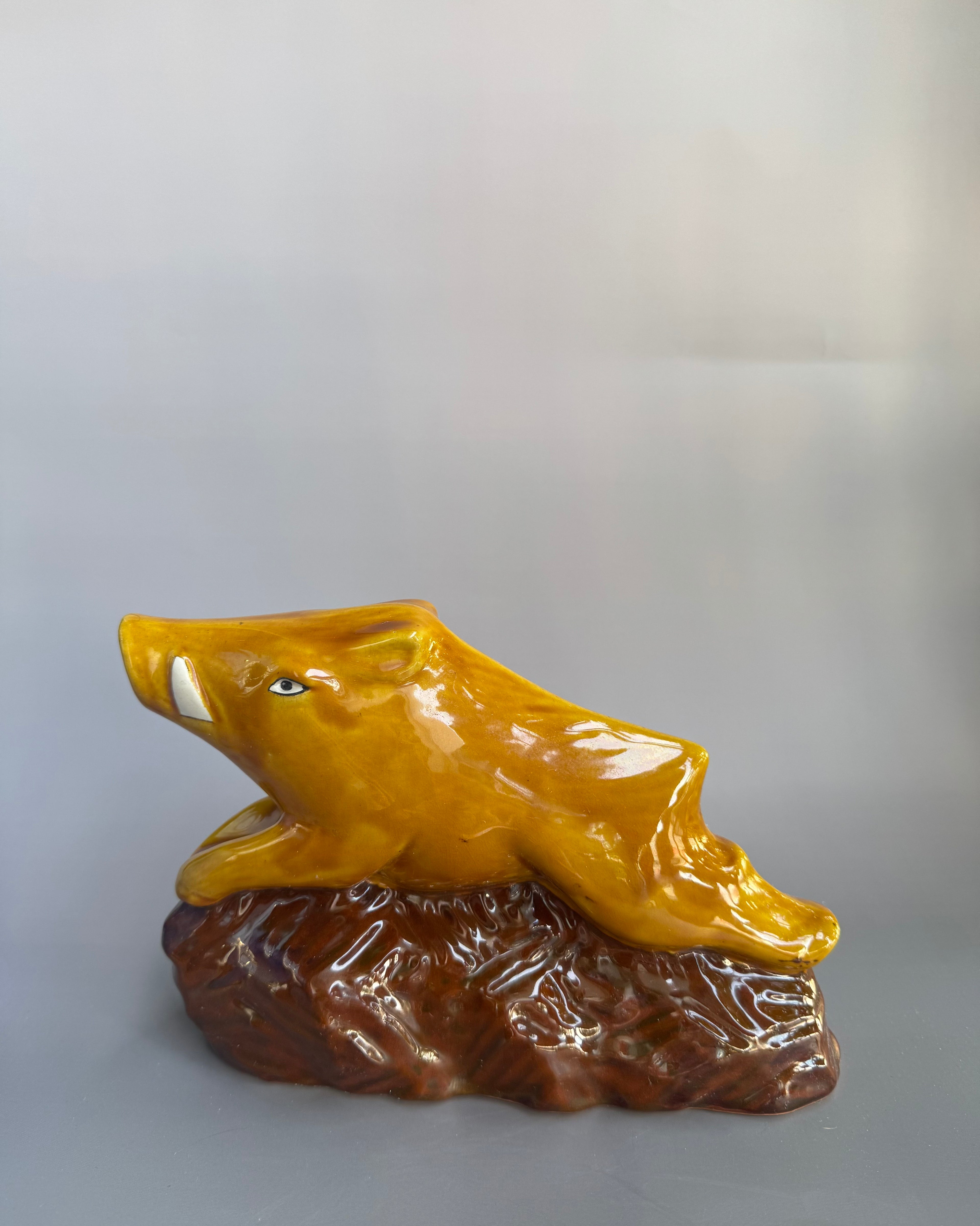 Yellow ceramic figurine on a brown base against a gray background