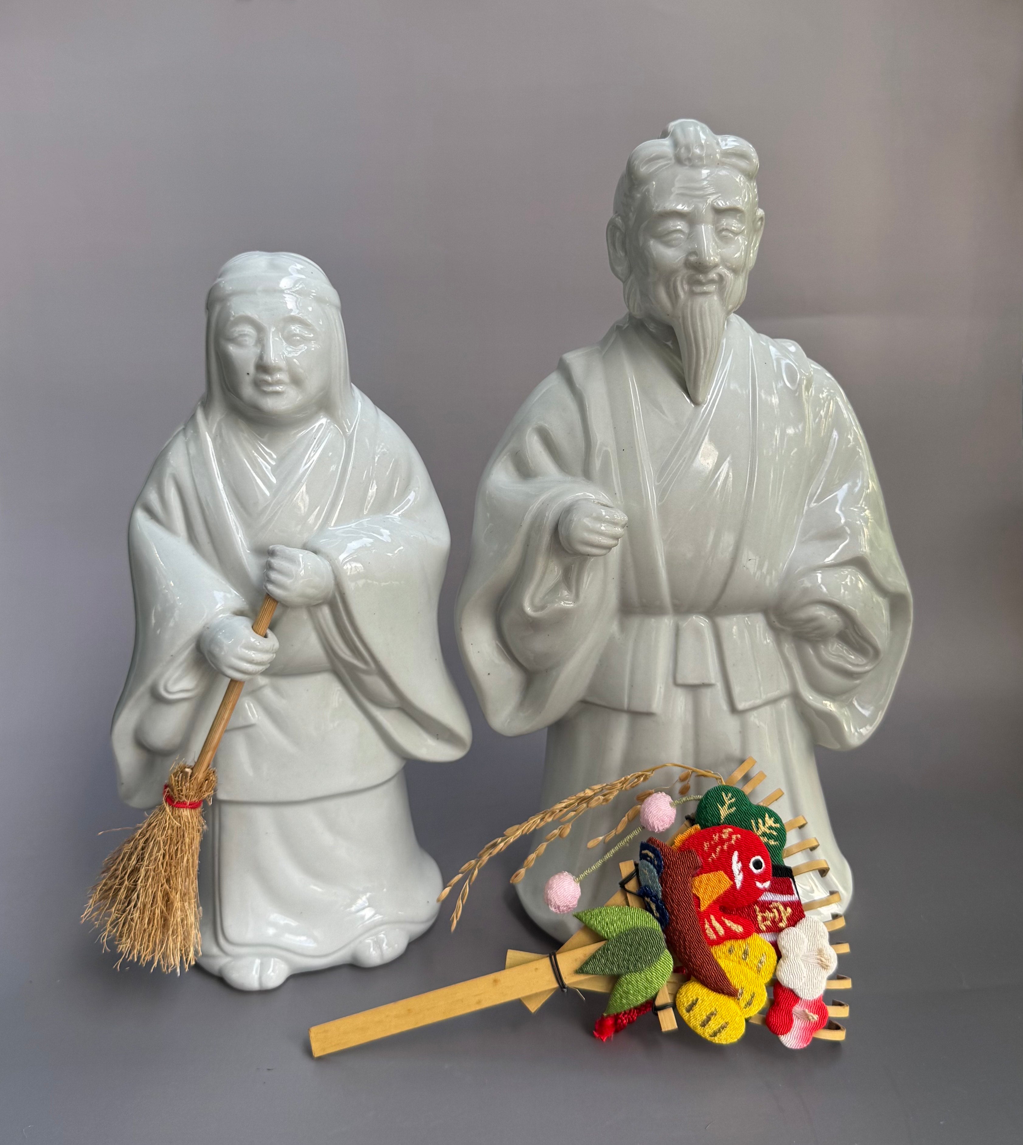Two ceramic figures of a man and a woman with a small decorative item on a gray background