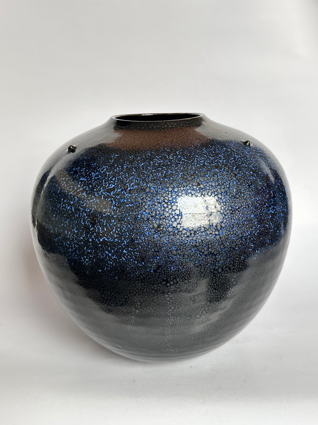 Glossy black and blue speckled vase on a white background