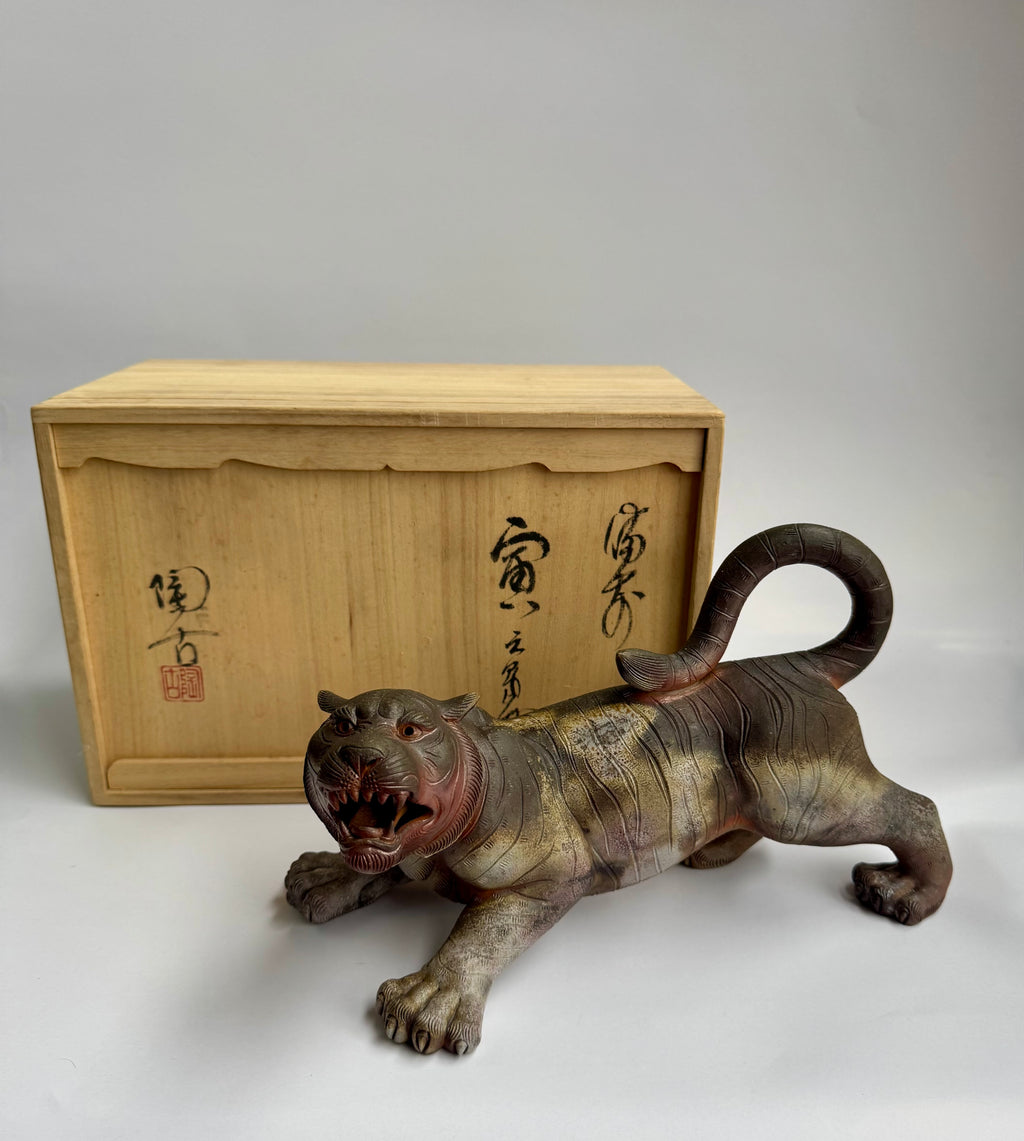 Vintage tiger figurine in front of a wooden box with Japanese text on a white background