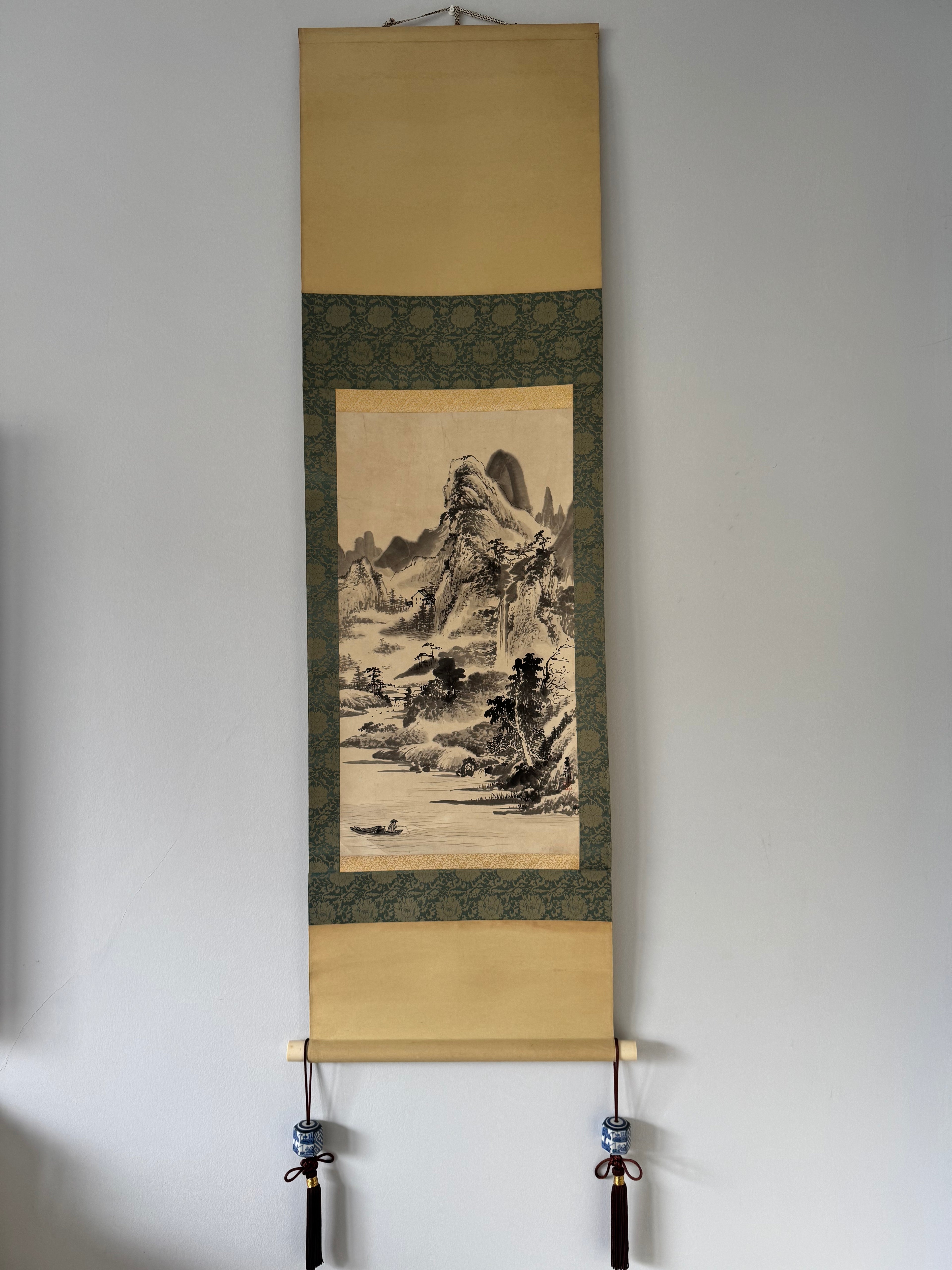 Traditional Chinese landscape painting on a scroll displayed against a white wall.