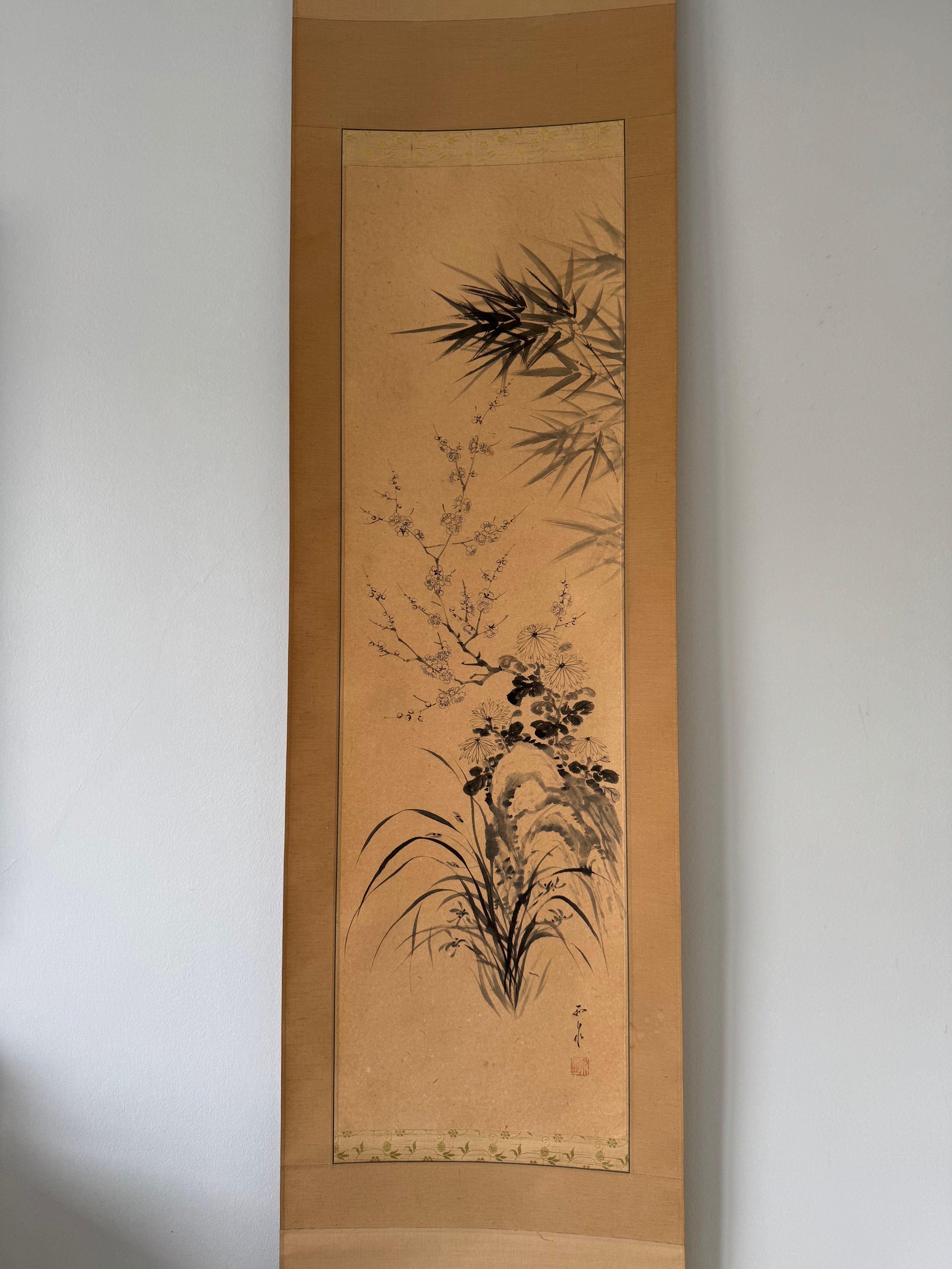 Traditional painting on paper with bamboo and floral elements, framed against a plain wall.