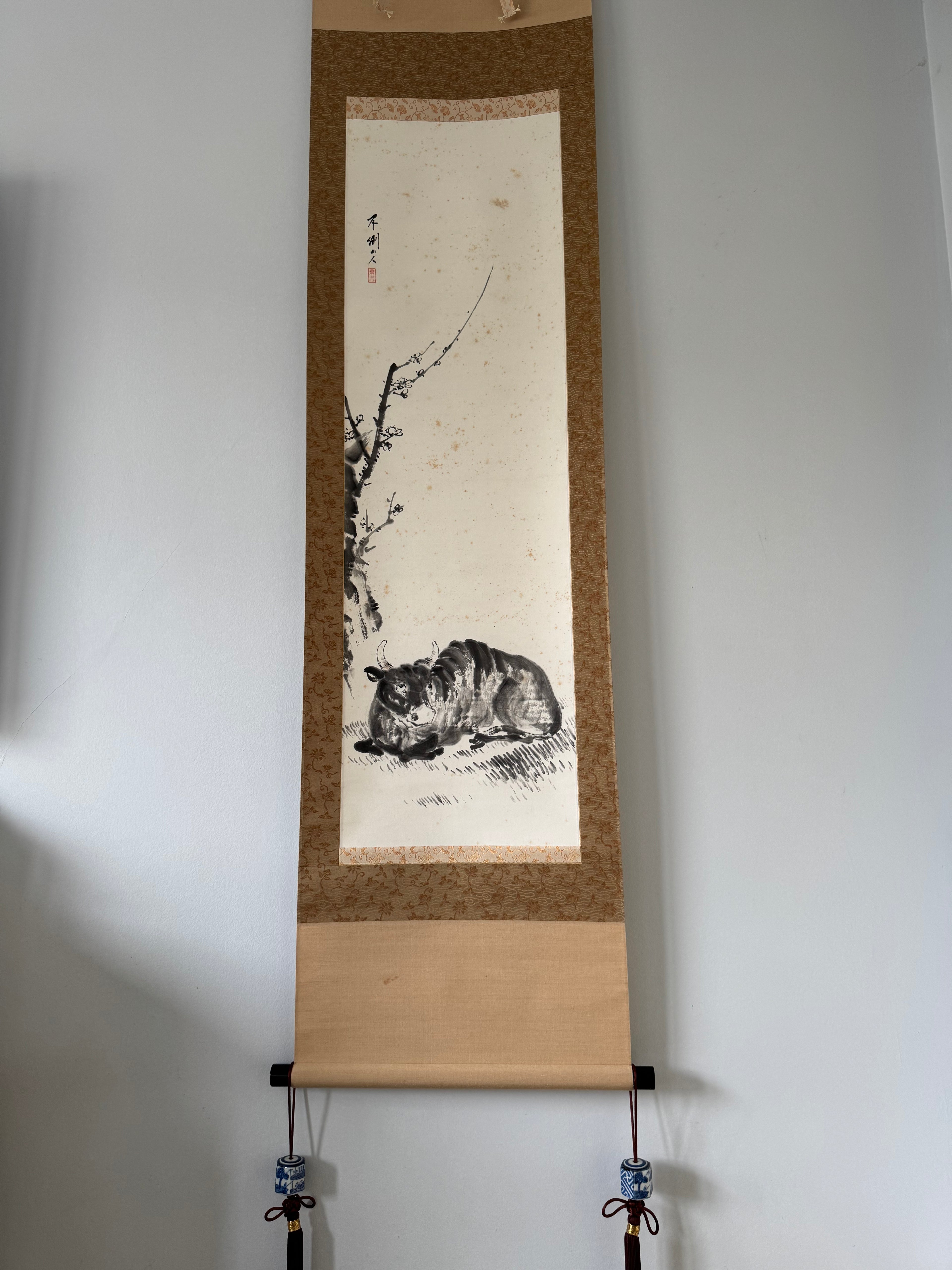 Traditional Chinese ink painting of a bird on a branch in a wooden frame against a white wall.