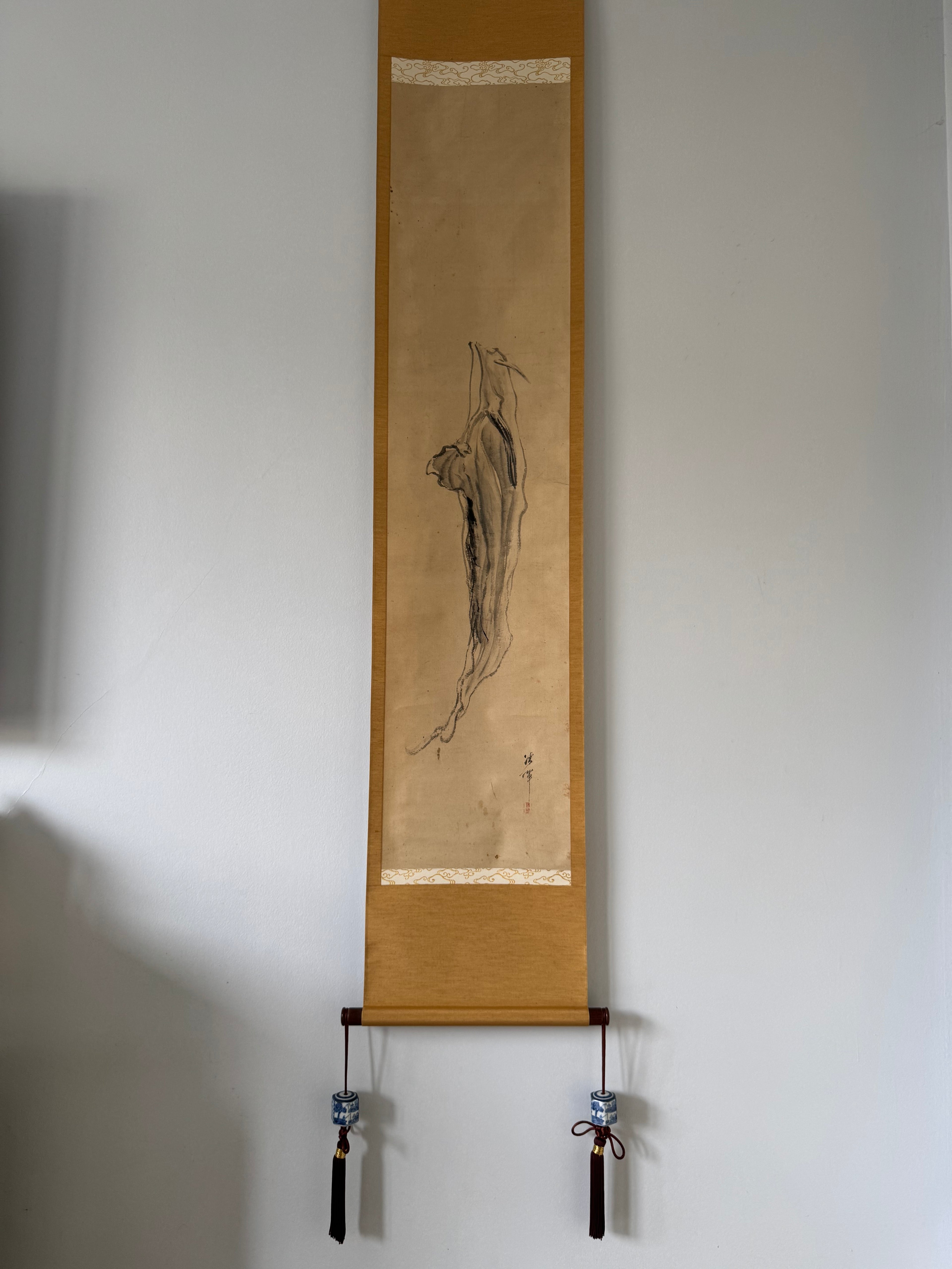 Traditional Chinese scroll with ink drawing on a plain wall