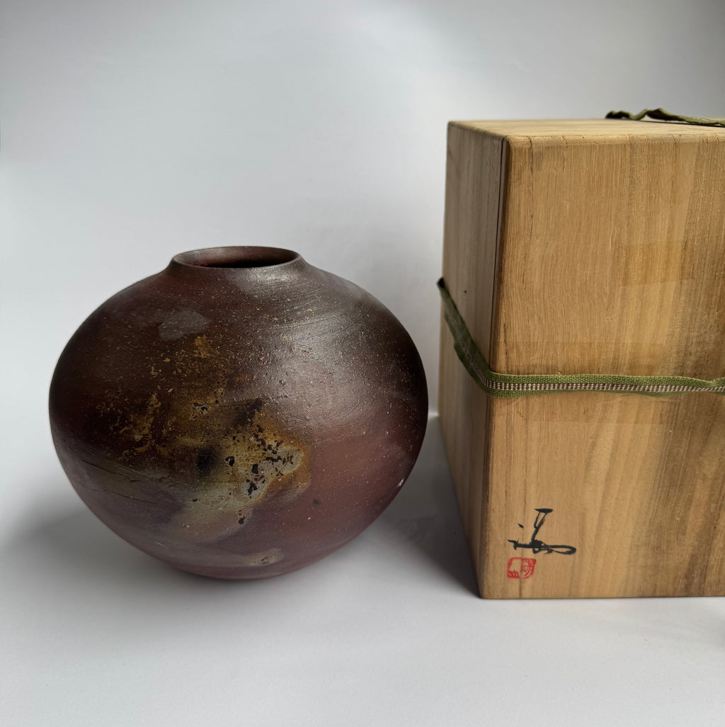 Brown ceramic vase next to a wooden box with a green string on a white background