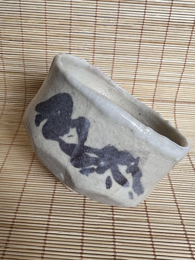 Ceramic bowl with black abstract design on a woven mat