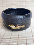 Black ceramic bowl with gold accent on a woven mat