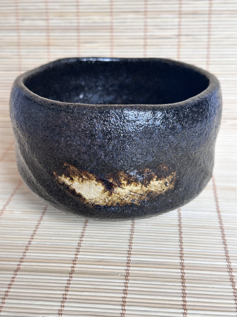 Black ceramic bowl with gold accent on a woven mat