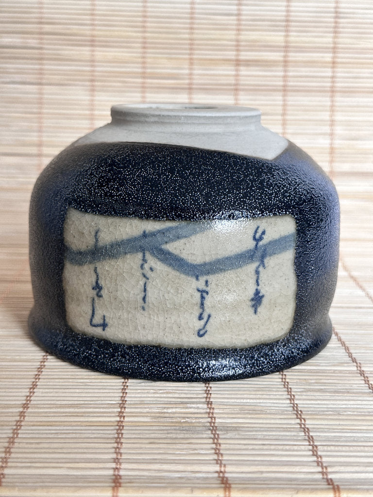 Ceramic jar with black glaze and blue designs on a woven mat background