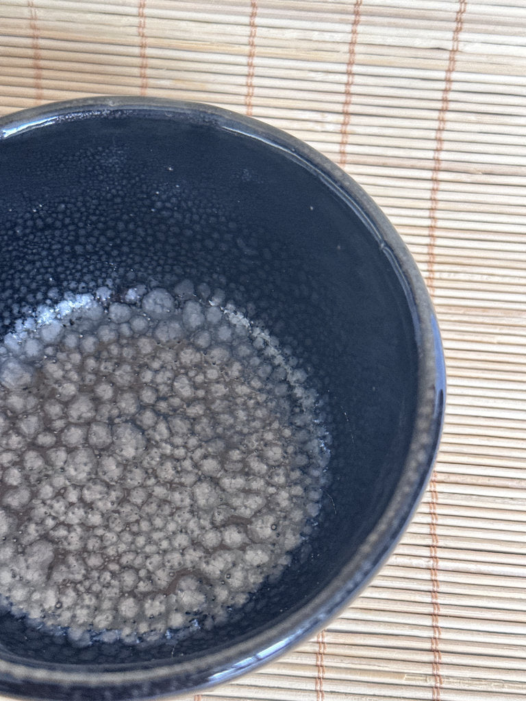 Black bowl with bubbling liquid on a woven mat