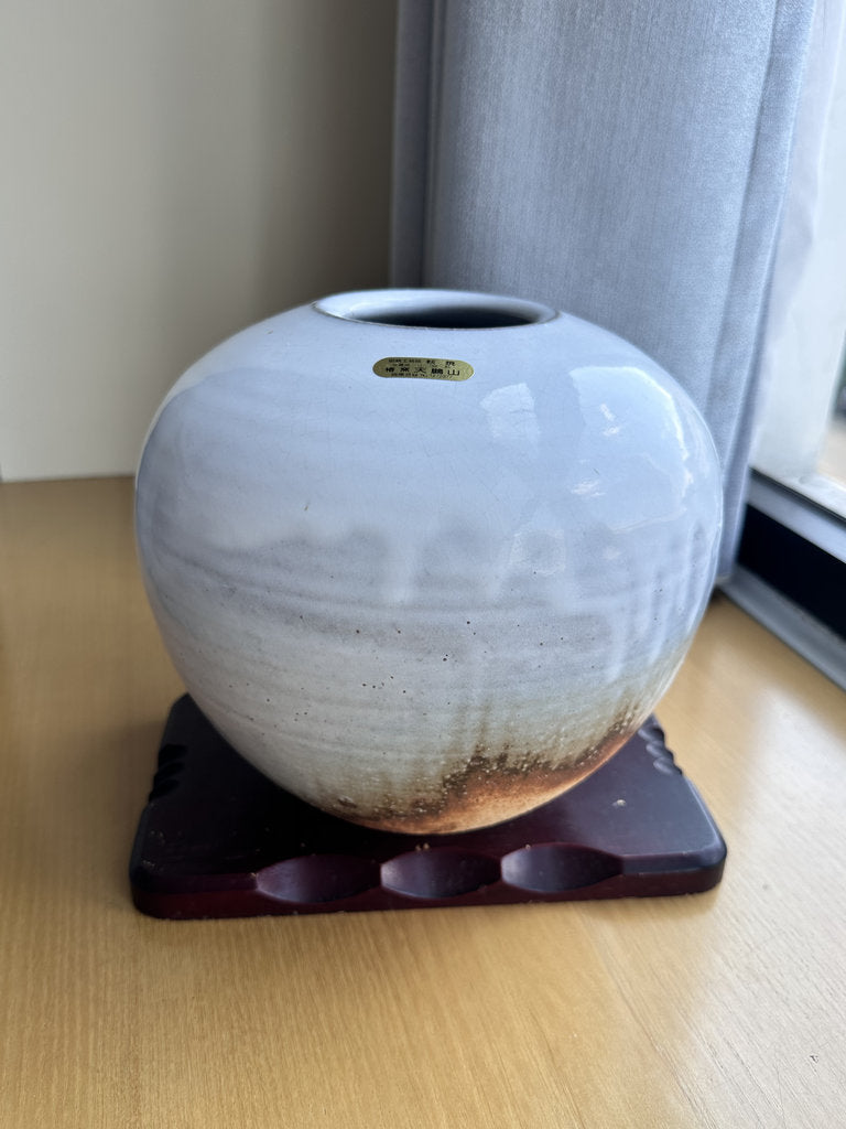 White ceramic vase on a wooden stand with a blurred background