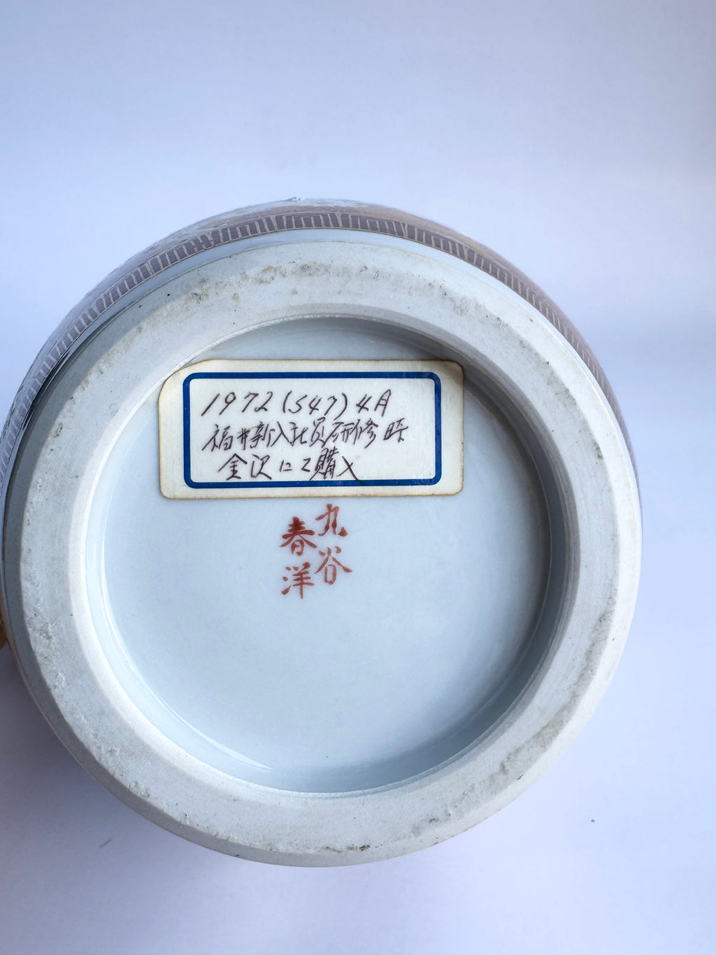 Bottom view of a ceramic vase with a label and signature on a white background