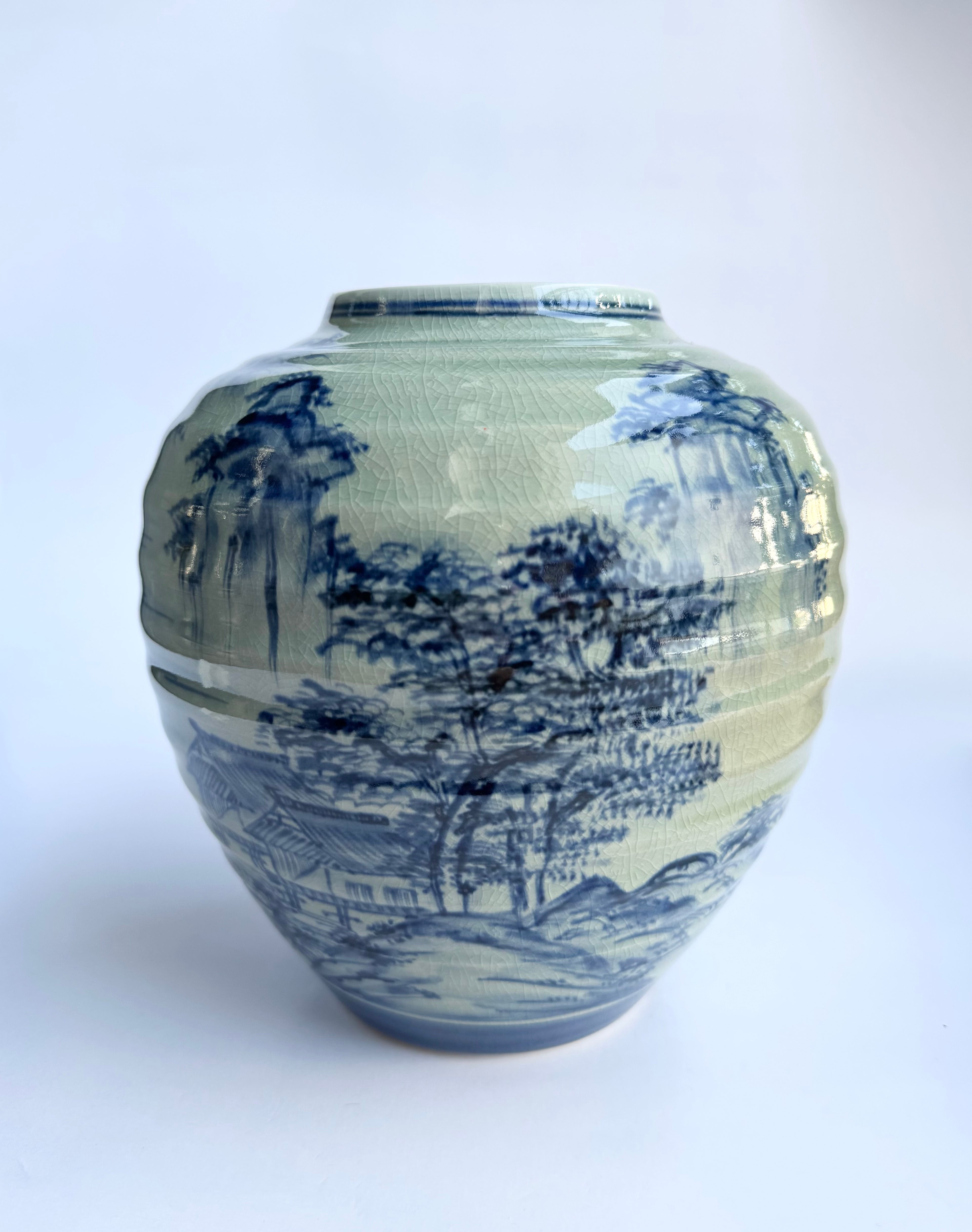 Ceramic vase with blue and white landscape design on a white background