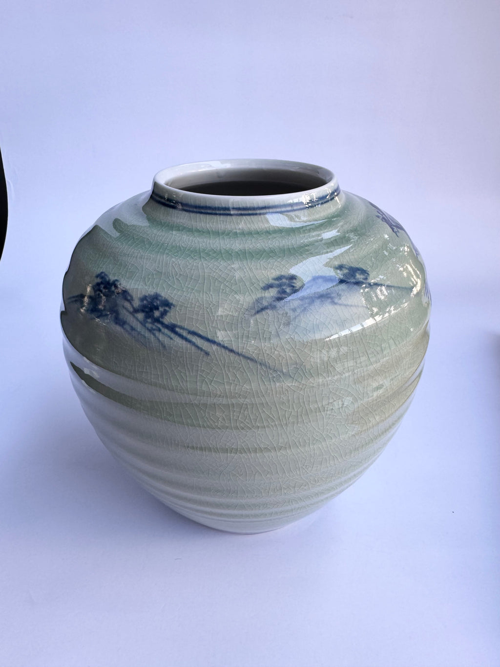 Green ceramic vase with blue floral patterns on a white background
