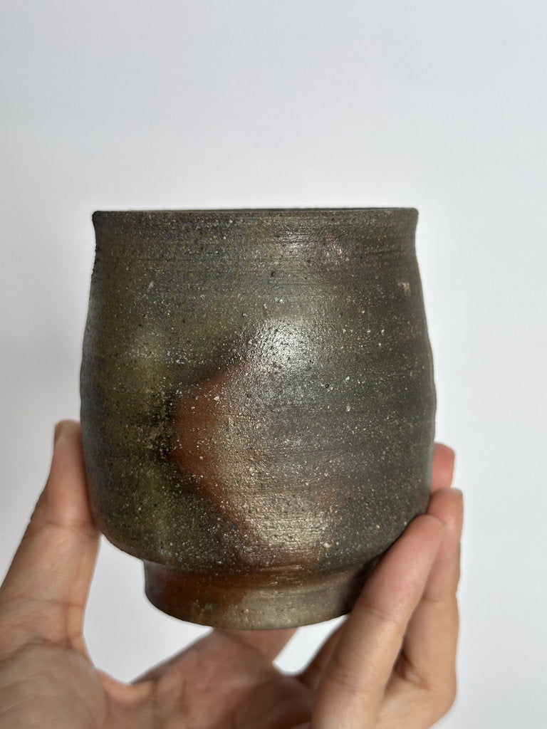Hand holding a rustic ceramic cup against a plain background