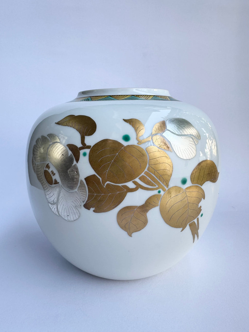 White ceramic jar with gold floral patterns on a light gray background
