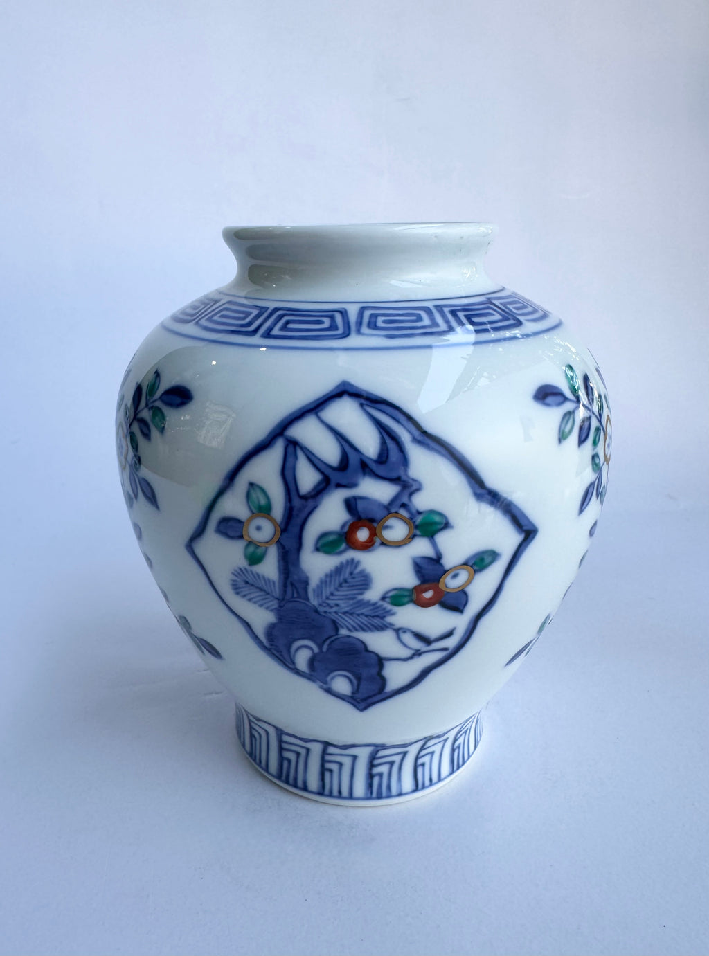 White ceramic vase with blue and green floral patterns on a white background