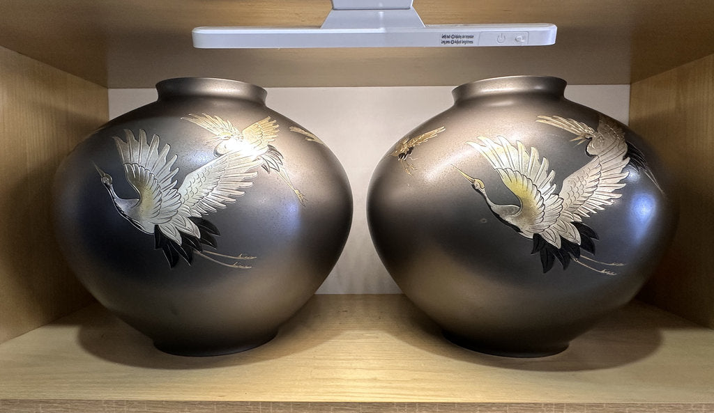 Two black vases with white crane designs on a wooden shelf.