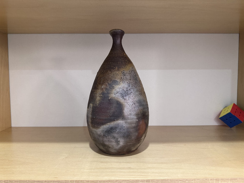 Brown ceramic vase on a wooden shelf with a white wall background