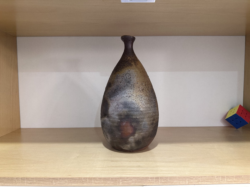 Decorative vase on a wooden shelf with a plain background