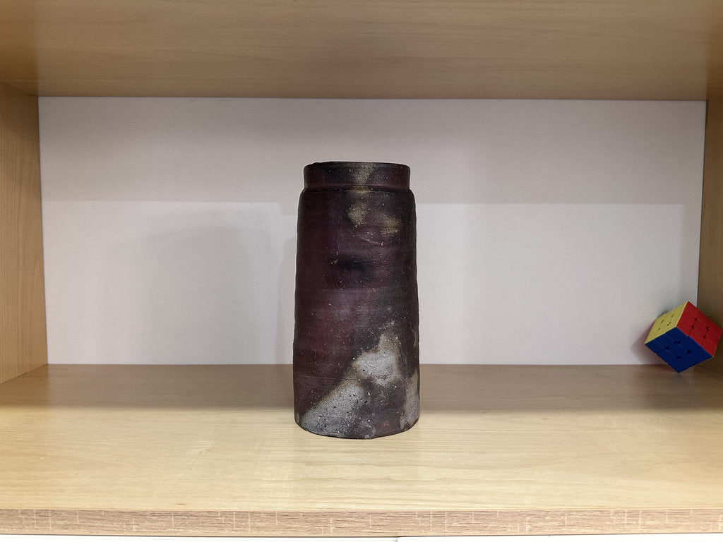 Cylindrical vase with a textured surface on a wooden shelf