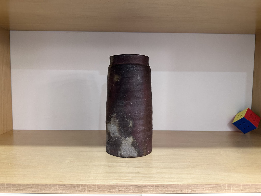 Cylindrical ceramic vase on a wooden shelf with a white wall background