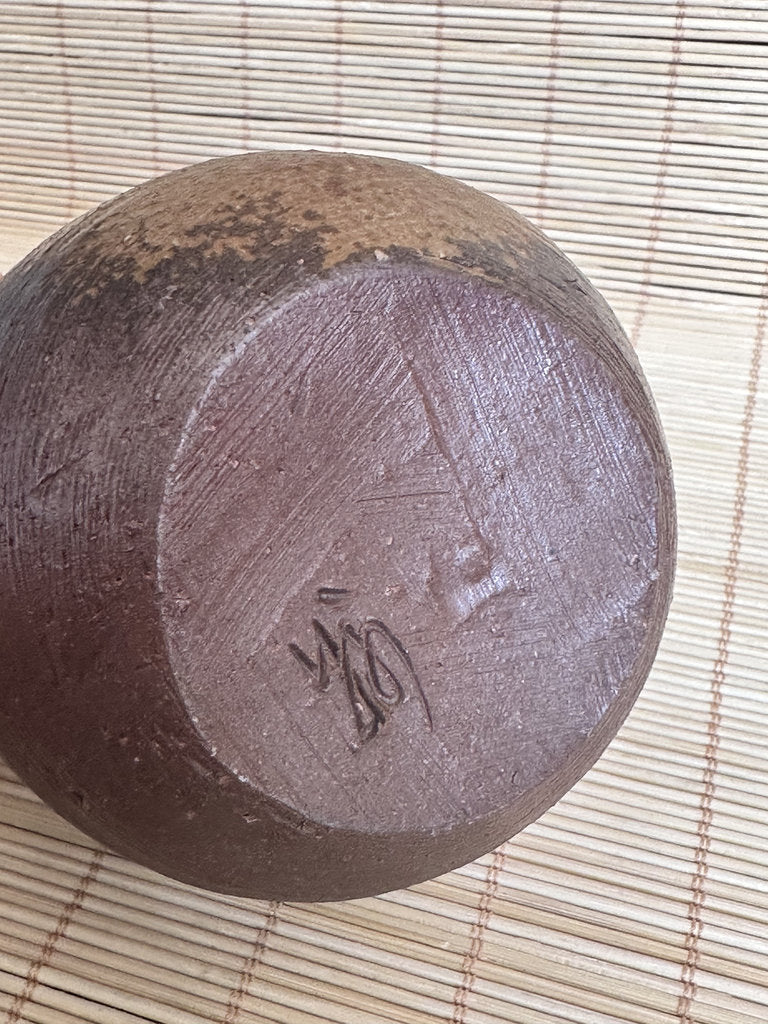 Dark brown ceramic bowl with a visible brand logo on a woven mat background