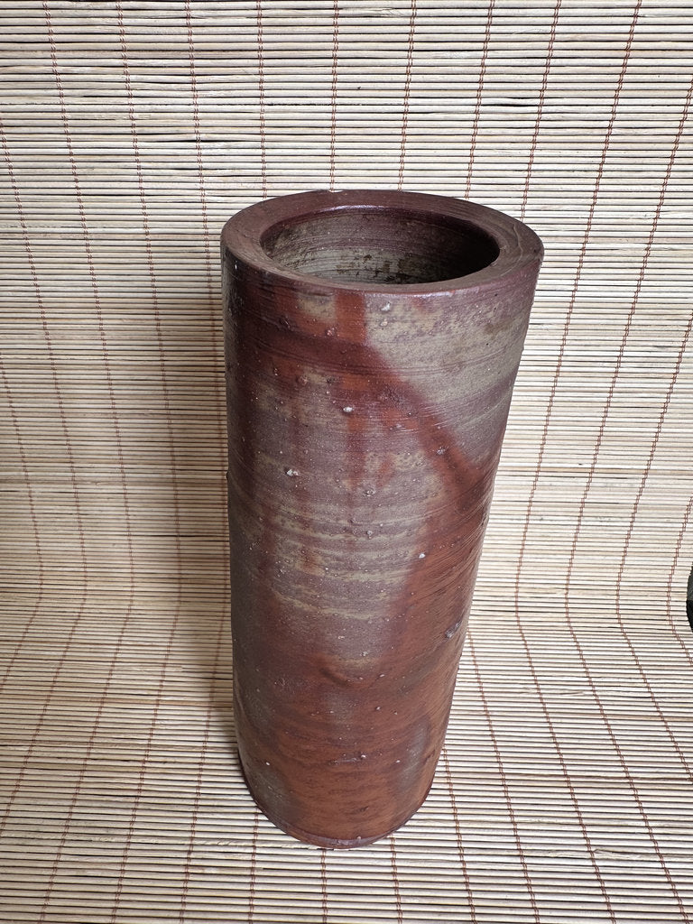 Cylindrical reddish-brown vase on a woven mat background