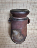 Brown ceramic vase with black top on a woven mat