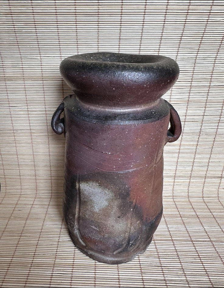 Brown ceramic vase with black top on a woven mat