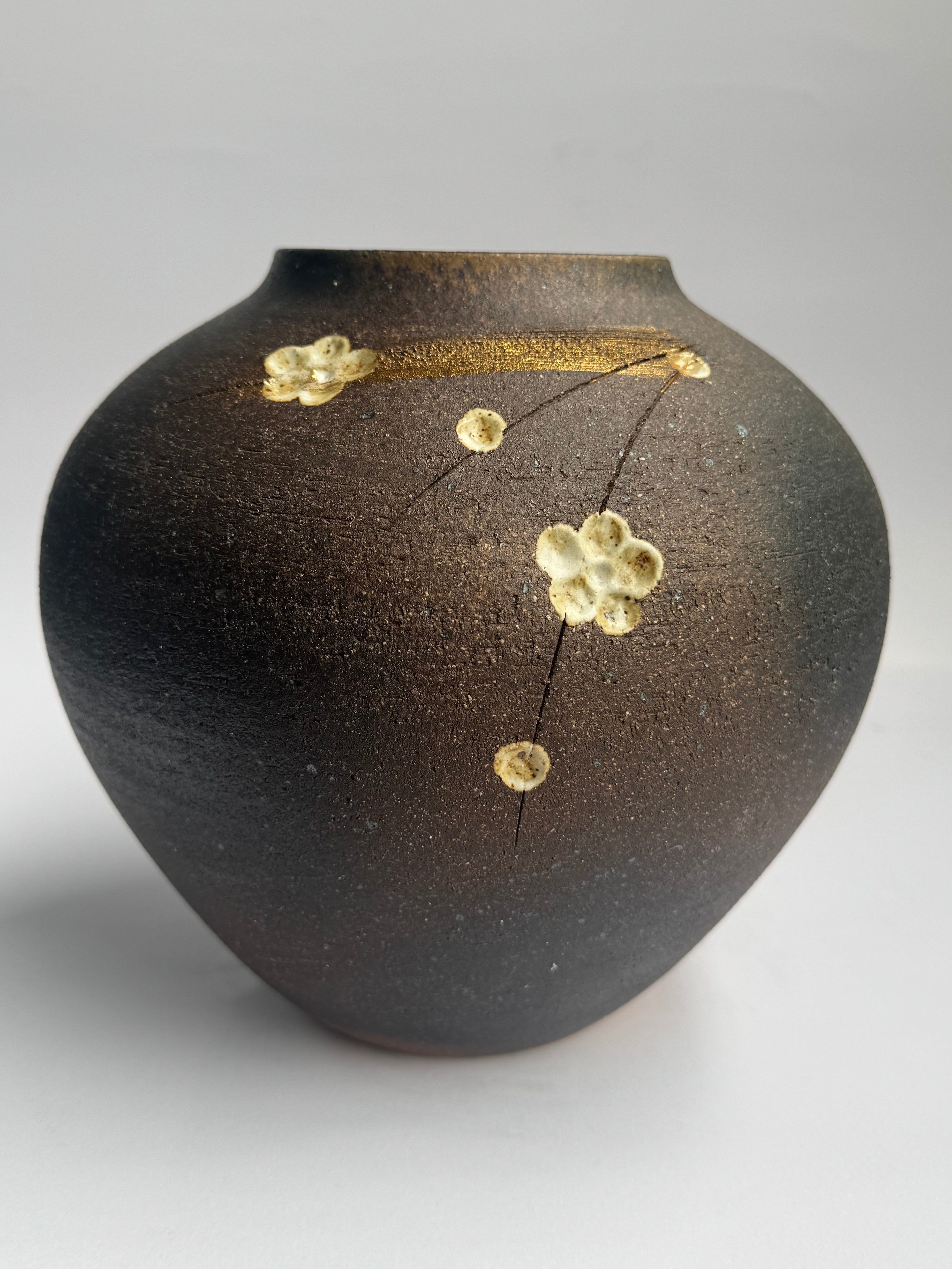 Black ceramic object with gold decorative elements on a gray background