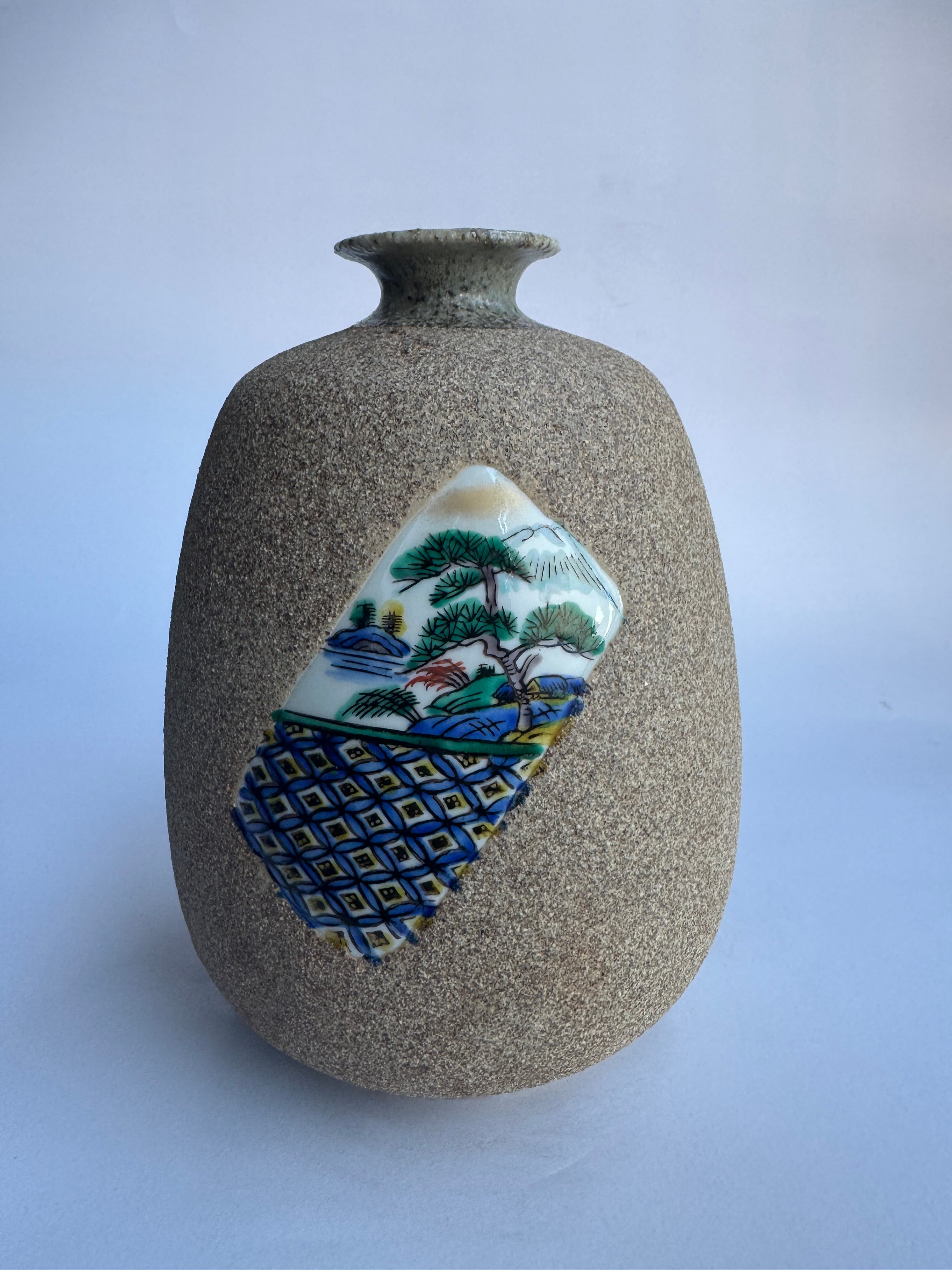 Decorative vase with textured surface and ceramic patch featuring a landscape design on a light gray background